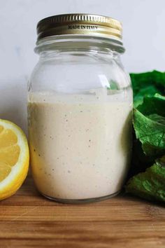 a glass jar filled with dressing next to a sliced lemon and lettuce leaves