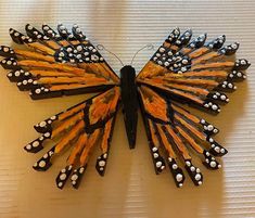 a butterfly made out of pencils sitting on top of a white surface with black and orange wings