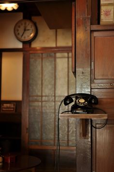 an old fashioned telephone sitting on top of a wooden table next to a wall clock