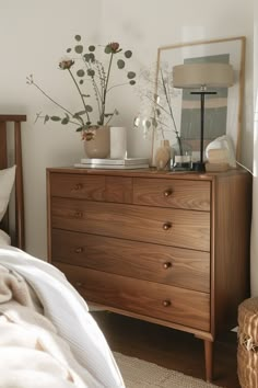 a bedroom with a bed, dresser and flowers on top of the dresser in front of it