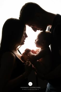 a man and woman holding a baby in front of a white background with the light coming through them