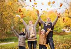 three adults and two children are throwing leaves in the air while standing on a leaf covered path