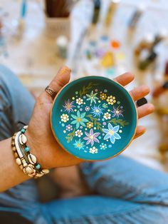 a person holding a bowl with flowers painted on it in their left hand and bracelets around her wrist