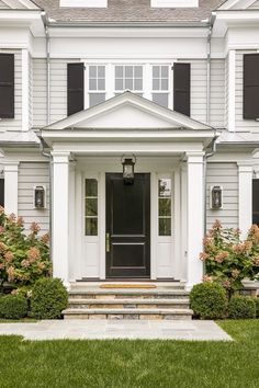 a white house with black shutters and a front door on the side walk leading up to it