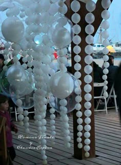 some white balloons are hanging from a wooden structure on a deck with people in the background