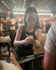 a woman standing in front of a crowd holding a cell phone and looking at it