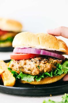 a hamburger with lettuce, tomato and onion on a black plate next to french fries