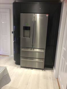 a stainless steel refrigerator and freezer combo in a kitchen with hardwood floors, white walls and black cabinets