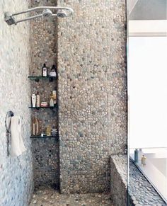 a bathroom with stone walls and flooring next to a bathtub, shower head and shelves