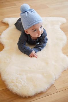 a baby wearing a blue hat laying on top of a white sheepskin area rug