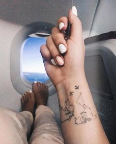 a woman's arm with a small world map tattoo on her left wrist, and an airplane wing in the background