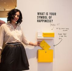 a woman standing in front of a white wall with yellow boxes on it and writing on the wall