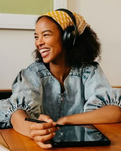 a woman sitting at a table wearing headphones and holding a cell phone in her hand