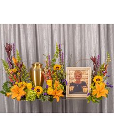 an arrangement of flowers and vases with a portrait on the wall behind them in front of a curtain