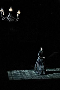 a woman standing in the dark under a chandelier