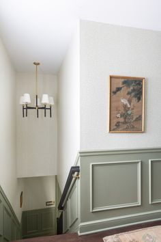 a painting hangs on the wall next to some green painted stairs in a house with white walls and wood paneling