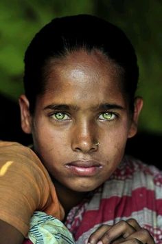 a young boy with green eyes is looking at the camera and has his hands folded over his shoulder