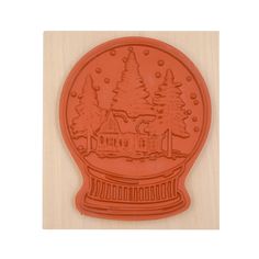 a red cookie mold with a house and trees in the background on a wooden surface