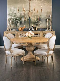 a dining room table with white chairs and a painting on the wall behind it,