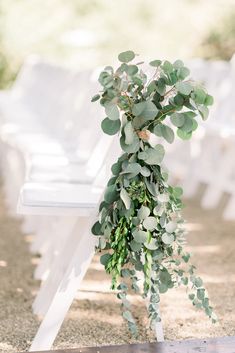 an outdoor ceremony with white chairs and greenery on the back of each chair,