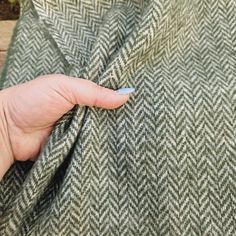 a person's hand is holding onto a green and white tweed fabric that has been stitched together