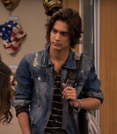 the young man is wearing a jean jacket and black striped t - shirt while holding a backpack