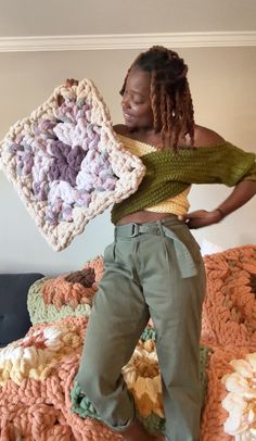 a woman standing on top of a bed holding a crocheted blanket