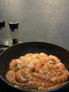 shrimp being cooked in a skillet on the stove with two glasses behind it,