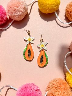 two pairs of earrings with flowers on them sitting next to pom - poms