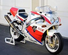 a red, white and blue motorcycle parked in front of a garage