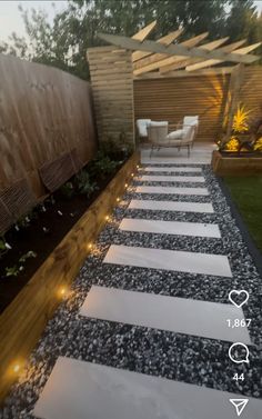 an outdoor walkway with lights on it and some plants in the back yard, next to a wooden fence