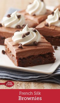 chocolate brownies topped with whipped cream and chocolate chips are on a white square plate