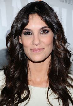 a close up of a person with long hair wearing a white shirt and smiling at the camera