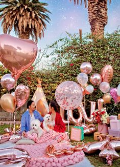 two people sitting on a blanket with balloons and presents