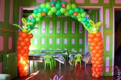 an arch decorated with balloons and flowers in the middle of a wooden floored room