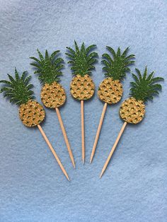 five pineapples on sticks with green leaves are arranged in the shape of palm trees