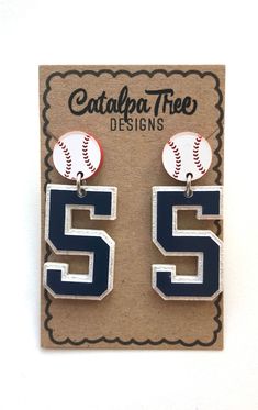 two baseball earrings with the number 55 on them, sitting in front of a card