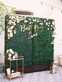 a green wall covered in flowers and greenery with the words best party ever written on it