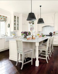 a white kitchen with two pendant lights hanging over the island and four chairs around it