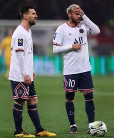 two soccer players are standing next to each other on the field with their hands in their ears