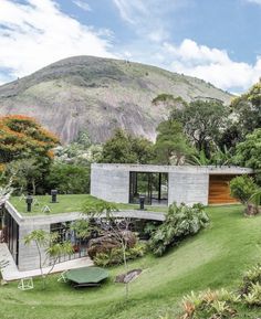 a house in the middle of a lush green field with mountains in the background and trees on either side