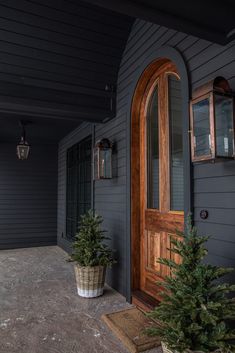 two potted trees sitting on the front porch of a house next to a door