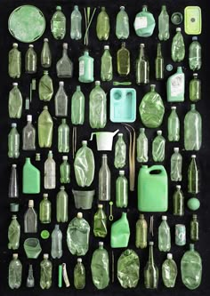 an assortment of green glass bottles and containers on a black surface with other items in the background