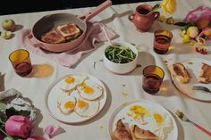 an assortment of breakfast foods on a table with pink flowers and teacups,