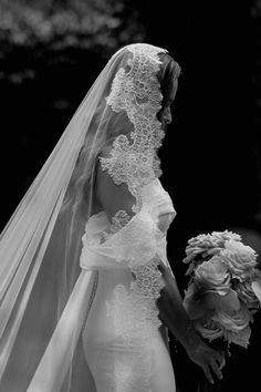 the bride is walking down the aisle with her veil blowing in the wind as she holds her bouquet