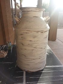 a large white vase sitting on top of a black table next to a building with sun shining through the windows