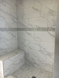 a bathroom with white marble walls and floor tiles on the shower wall, along with a bench in the corner