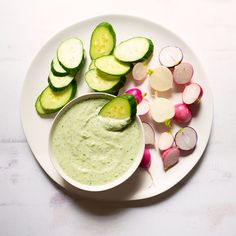 a white plate topped with cucumber and radishes next to a bowl of dip