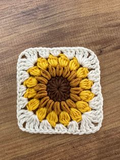 a crocheted square with a yellow and brown flower in the center on a wooden surface