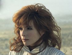 a woman with long red hair standing in the desert